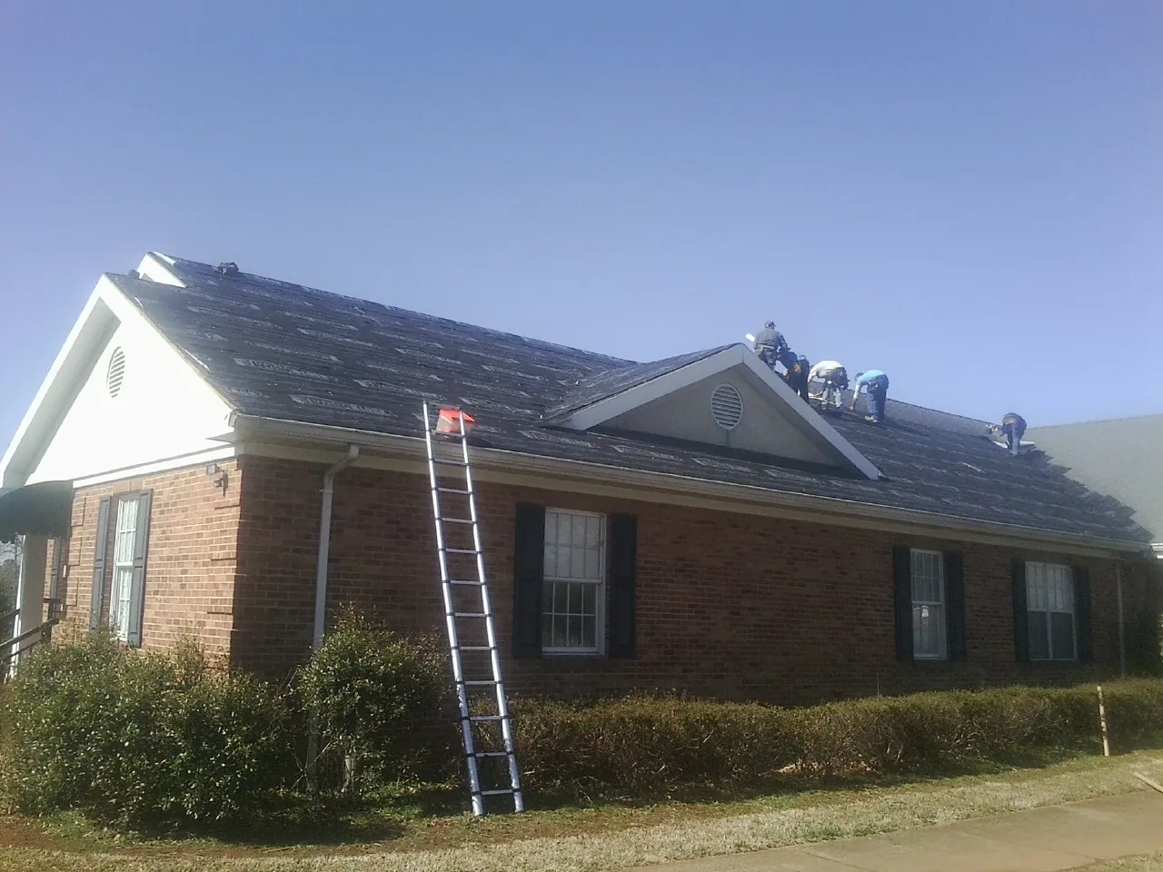 Crew tearing shingles off a brick ranch roof with a ladder set — Emergency Roof Repair work by our crew in Coyote