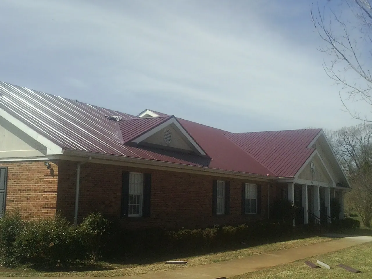 Red metal roof with gabled entries on a long brick building, from a Hail Damage Roof Repair job in Coyote