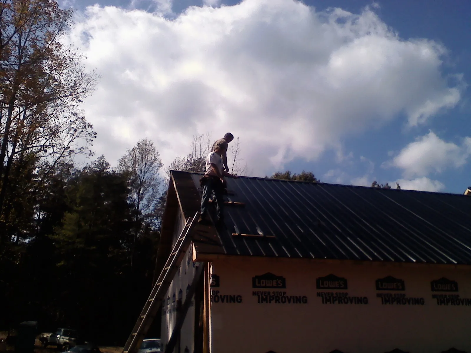 Roofer fastening dark metal panels high against a cloudy sky, from a Roof Inspection job in Coyote